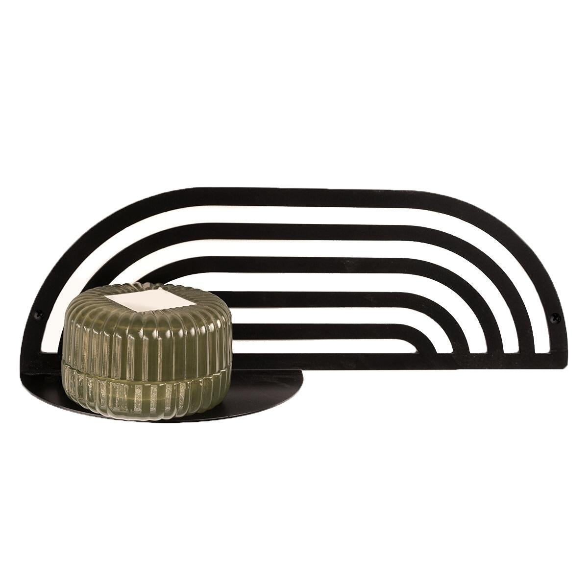 Black metal decorative shelf with a modern, arch design, holding a green candle holder on a round base.
