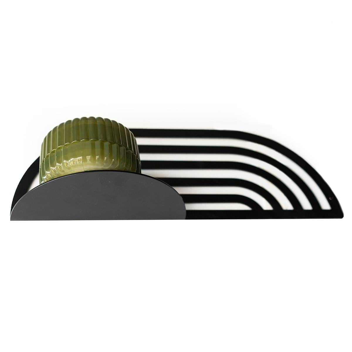 Decorative metal rack with an arched design, holding a small, rounded, ribbed container placed on its surface. The rack features parallel bars creating a sleek, modern look.