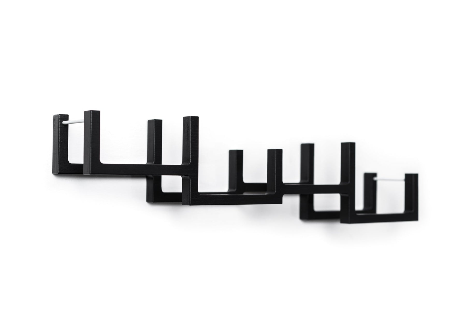 Close-up of a black geometric wall-mounted toilet paper holder with a series of square frames and metal bars to hold multiple rolls.