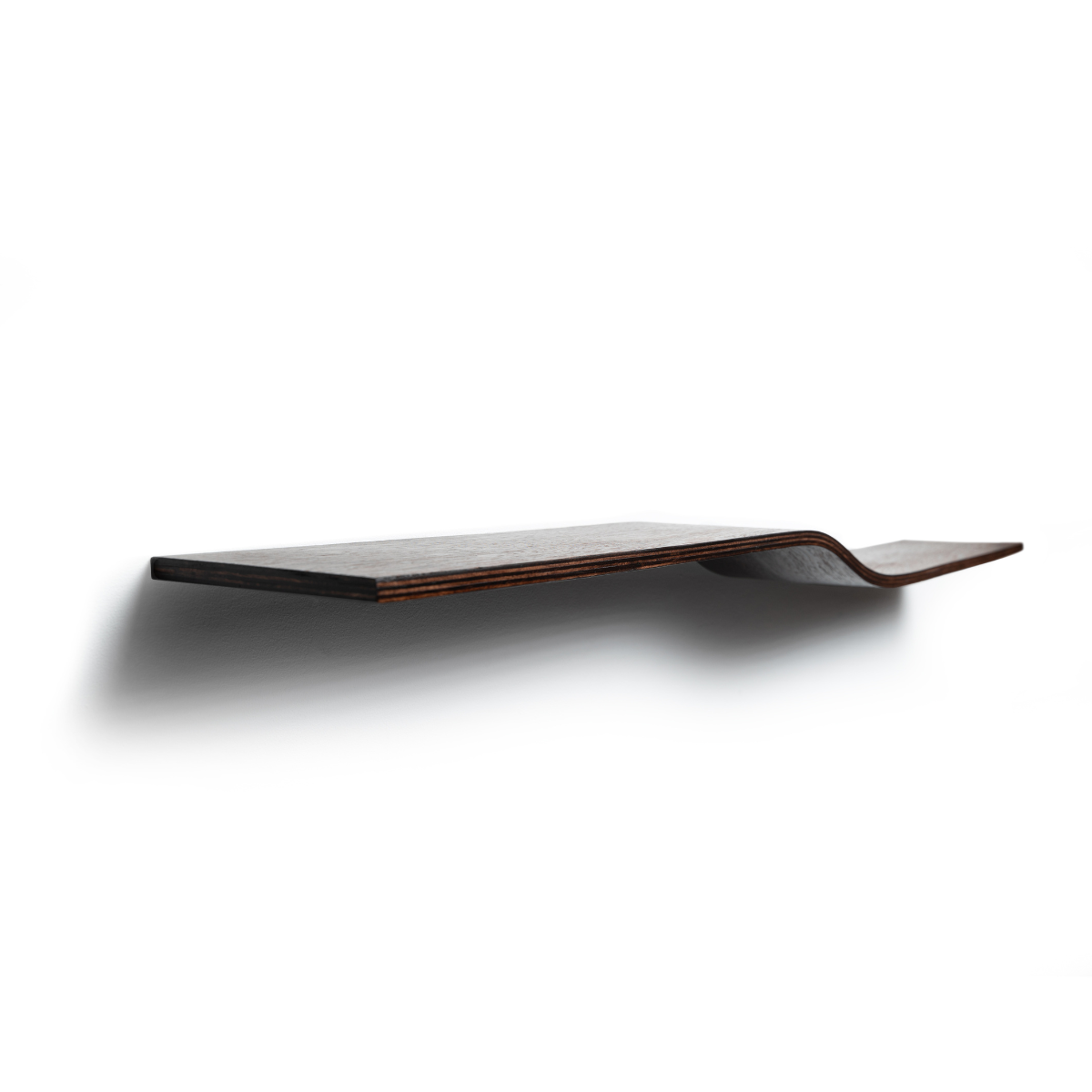Side view of a dark wooden, floating shelf with a slight curve in the middle, mounted on a white wall. The side edge of the shelf is stained, highlighting the natural wood grain.