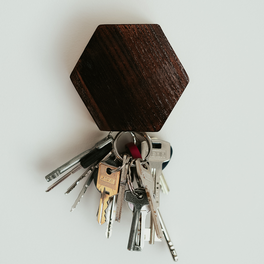 Close-up of a dark brown magnetic wooden key holder with several metal keys attached.