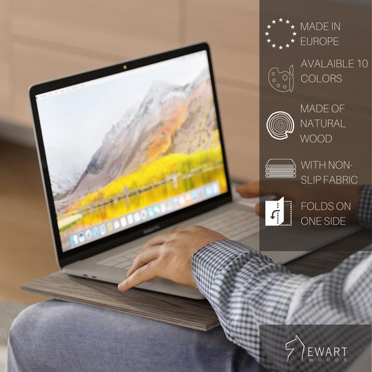 A person using a laptop on a wooden lap desk with gray fabric. Features listed: Made in Europe, 10 color options, natural wood, non-slip fabric, folds on one side. Ewart Woods logo is visible in the corner.