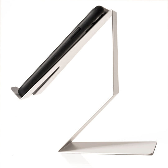 A smartphone positioned on a sleek, white cell phone holder, viewed from the side to show its angled design and minimalist structure.