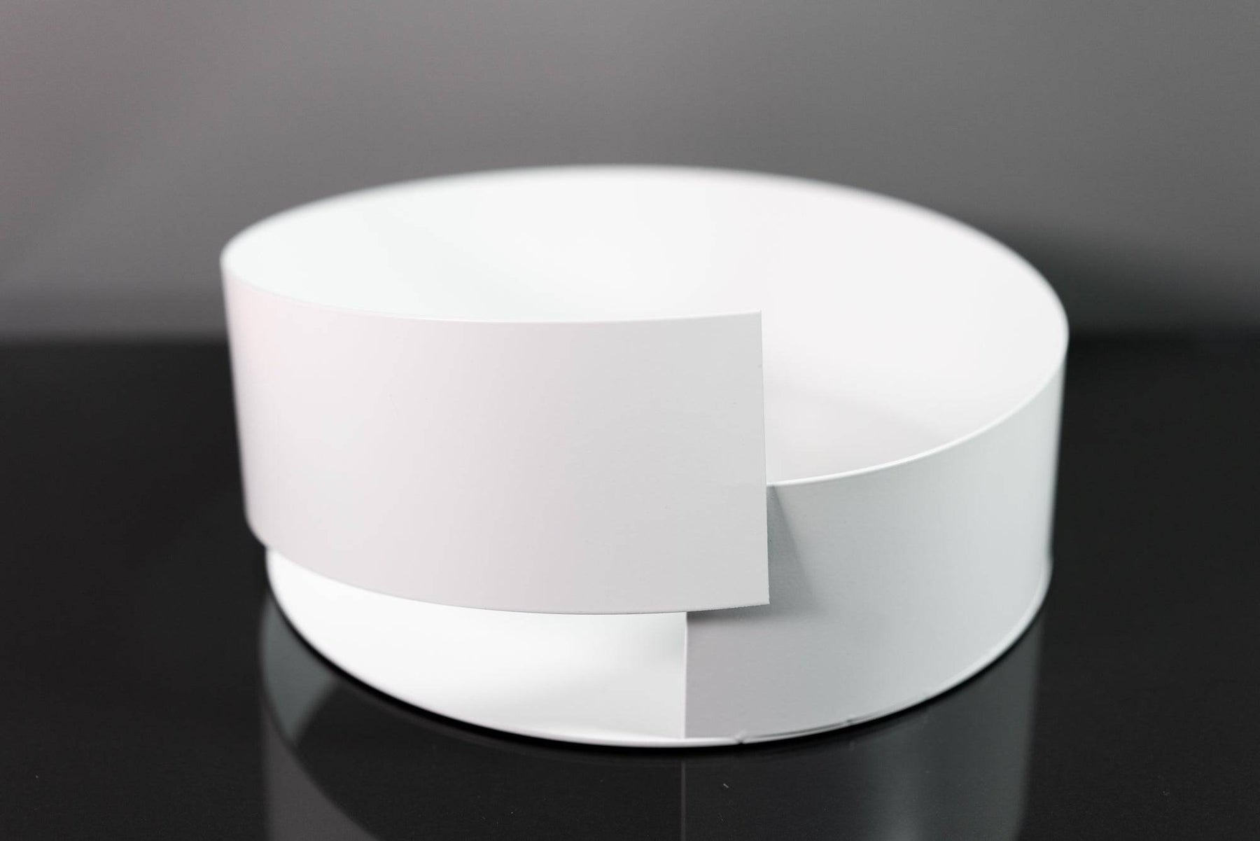 Sleek white metal bowl featuring a minimalist overlapping design, displayed on a glossy black surface for a modern aesthetic.